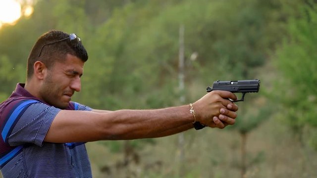 Young arab man is shooting from a gun, close up. Slow motion