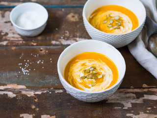 Two ceramic bowls with pumpkin cream-soup on an old wooden background