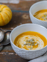 Two ceramic bowls with pumpkin cream-soup on an old wooden background