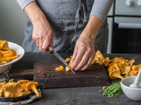 Woman is cutting fresh chanterelles on the boards in the kitchen