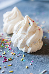 Beautiful italian meringue cookies on dark gray background with colorful sprinkles. Selective focus, close up