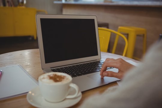 Cropped hand of businesswoman with coffee using laptop