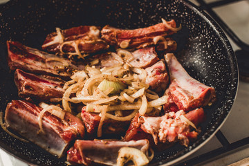 Roasted pork ribs with onion in frying pan, top view