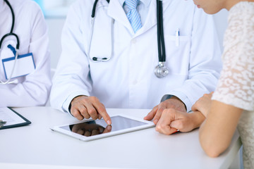 Doctor and  patient talking while sitting at the desk in office. Physician pointing into touch pad computer or tablet. Medicine and health care concept