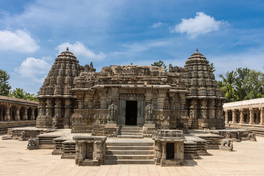 Mysore, India - October 27, 2013: Beige stone central sanctuary, called Trikuta, of Chennakesava Temple in Somanathpur under bluish sky. Fully decorated with statues and friezes. Tops of green palms.