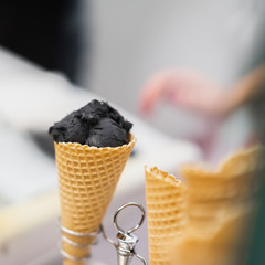 Close-up of waffle cone with ball of trendy black ice cream. Delicious cooling portion on hot day and just for fun. Selective focus. Real scene in store. Copy space