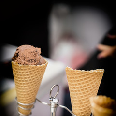 Close-up of waffle cone, horn with balls of chocolate, coffee soft ice cream, dark background. Popular delicacies for adults and children. Selective focus. Real scene in store