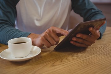 Mid section of man with coffee using tablet in cafe