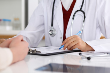 Close up of a female doctor filling up  an application form while consulting patient