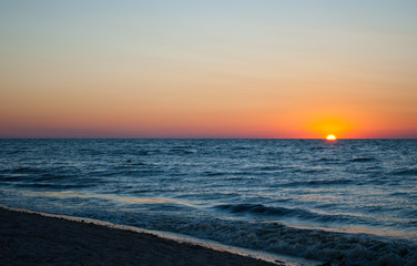 Beautiful sunrise over the sea, orange red sun, purple blue and pink sky without clouds, blue sea, sand wave vacation