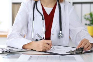 Close up of a female doctor filling up  an application form while sitting at the table