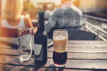 A large glass and a bottle of dark beer on the background of the pub on a wooden table. Tinted glass. Copy space. The horizontal frame.