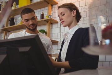 Female owner with waiter using cash register in cafe