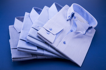 A set of 4 men's shirts in blue tones, folded on a blue background.
