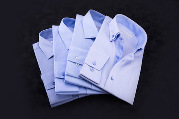 A set of 4 men's shirts in blue tones, folded on a black background.