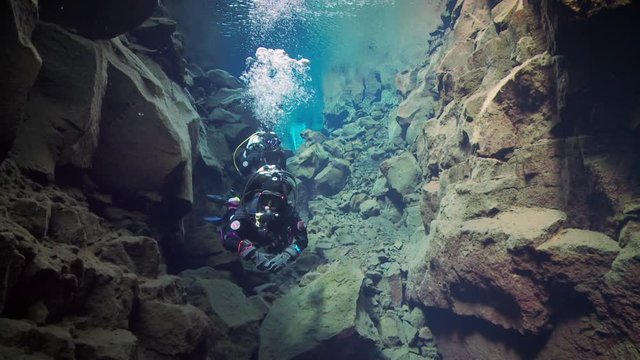 Two scuba divers swimming deeper into deep rocky trench