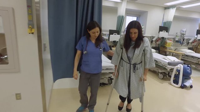 Nurse helps a female patient on crutches walk through hospital.