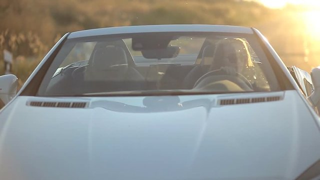 beautiful sexy girl with long hair in a leather jacket and leather pants in sunglasses gets out of the car at sunset