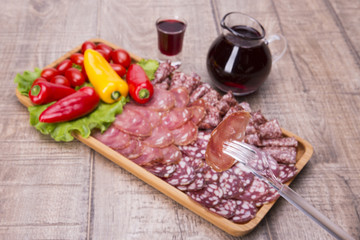 Set of meat delicatessen, tomatoes and peppers, wine on a wooden table.