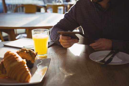 Mid section of businessman with breakfast using tablet in cafe