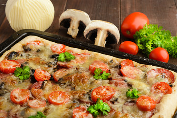 Homemade pizza with tomatoes, mushrooms, sausage and cheese over wooden background