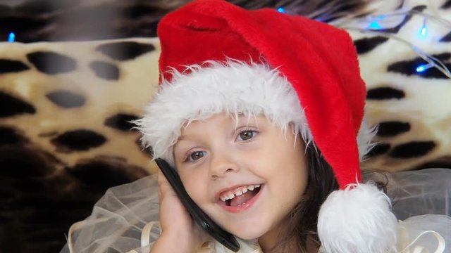 Happy child in Christmas with a mobile phone. A little girl in a Santa Claus hat speaks on the phone.