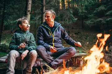 Father and son roast marshmallow candies on the campfire in forest