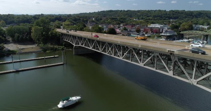 A reverse aerial view of traffic traveling on a bridge on Route 51 in Western Pennsylvania while a recreational boat passing underneath.  	
