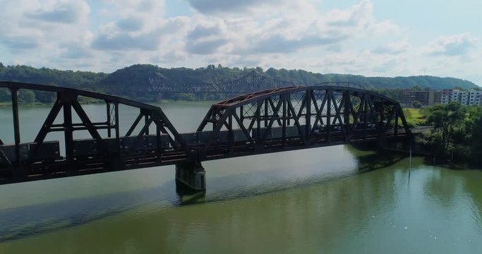ROCHESTER, PA - Circa September, 2017 - A forward high angle rising aerial establishing shot of a cargo train traveling over a railroad bridge in Western Pennsylvania. 