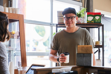 man receiving coffee at coffee shop at counter smiling at camera