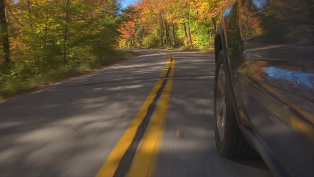 HYPERLAPSE TIME LAPSE Black SUV car tyre driving along double yellow line road past colorful trees on autumn day. Detail of car tire spinning while driving through bright autumn forest in sunny fall. 