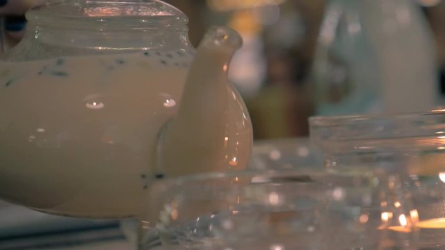 Close-up shot of woman taking a glass pot from candle heating and pouring masala tea into a glass cup