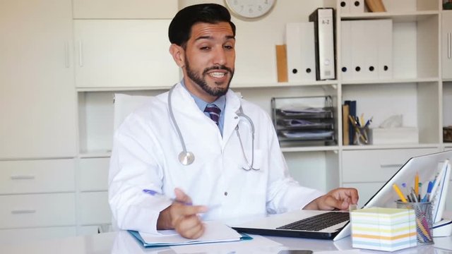 Doctor is working with documents in laptop in his work place
