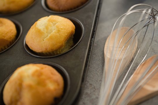 Close up of muffins in tin by wooden spoon and wire whisk