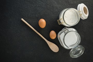 Overhead view of wooden spoon by eggs with sugar and flour in 