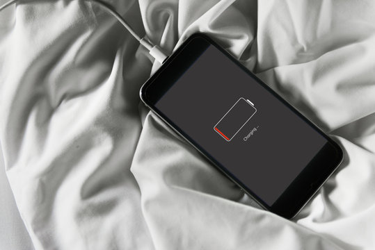 Closeup of dead mobile phone charging lying on white fabric background