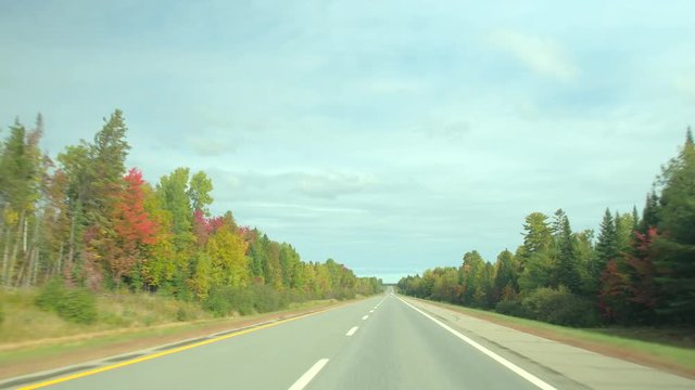DRIVER'S POV: Driving on empty highway trough beautiful autumn forest with red, yellow, green trees. FPV people on leaf peeping road trip traveling along an empty interstate past colorful autumn trees