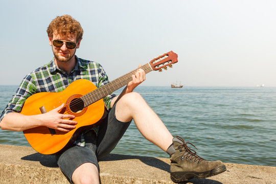 Young man hipster playing guitar by sea ocean.