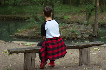 An imaginary boy is sitting on a bench in nature turned back