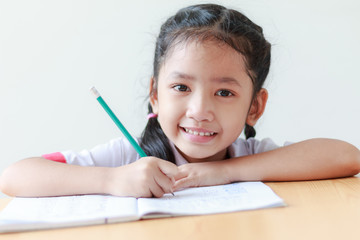 Portrait of Asian little girl in Thai kindergarten student uniform doing homework and smiling with...