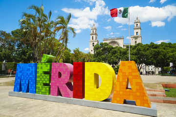 MERIDA, MEXICO - MAY 23, 2017: Colorful sign Merida with mexican flag and cathedral on a street in sunny summer day - obrazy, fototapety, plakaty