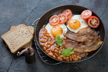 English breakfast with fried bacon, chicken eggs, beans in tomato sauce and tomatoes, horizontal shot