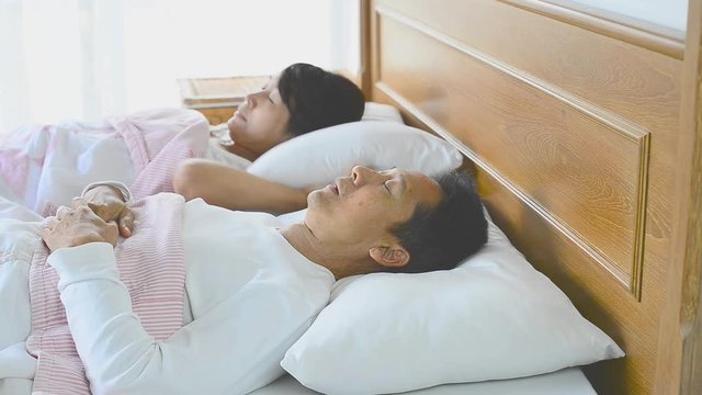 Sleep apnea man snoring and choking loud ,waking his wife up during the night, closing ears with pillow . Snoring with choking sound symptom is called obstructive sleep apnea,healthcare concept.


