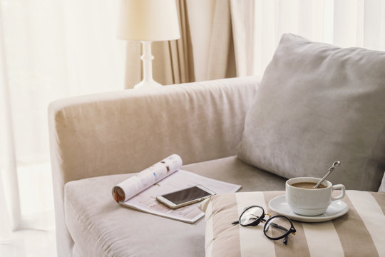 Cup of coffee with glasses on sofa in living room