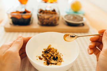 Healthy breakfast bowl. Yogurt, granola, seeds, fresh and dry fruits and honey in blue ceramic bowl in woman' s hands over table with strip tablecloth background. Clean eating, dieting food concept