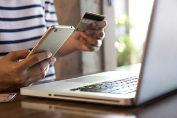 Hands holding credit card, mobile phone and using laptop. Online shopping, Travel booking concept. Selective focus.