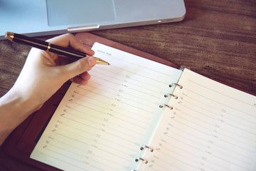 Hand of businesswoman writing on paper in office. Writing notes and planning her schedule.