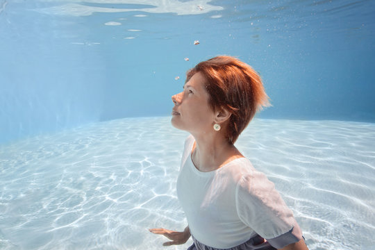 young woman in blue and white dress swim and dive underwater floating pool with transparent water in Beautiful Mysterious Underwater World. Fantastic Fairy dreamy fashion. Water safety class