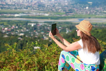Fototapeta premium young woman in a hat from the sun takes a photograph with a tablet in the mountains