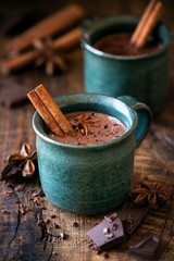 Heiße Schokolade mit Zimtstange, Anisstern und geriebenem Schokoladenbelag in festlichem Weihnachtsambiente auf dunklem rustikalem Holzhintergrund
